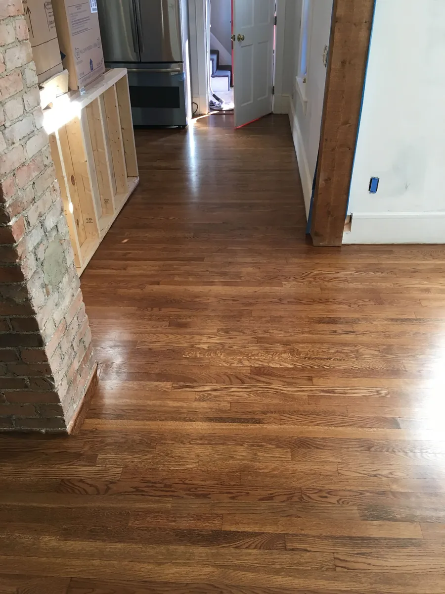 Refinished oak floor with a glossy coat in a hallway beside exposed brick